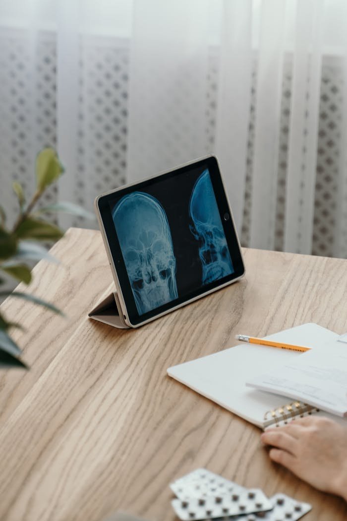 Tablet showing X-rays on wooden desk, pen and notebook nearby.