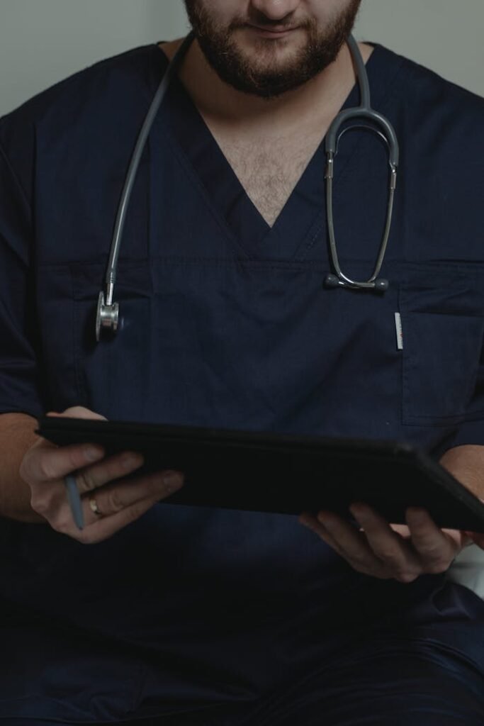 Doctor in navy scrubs with stethoscope, holding a digital tablet, focuses on patient information.
