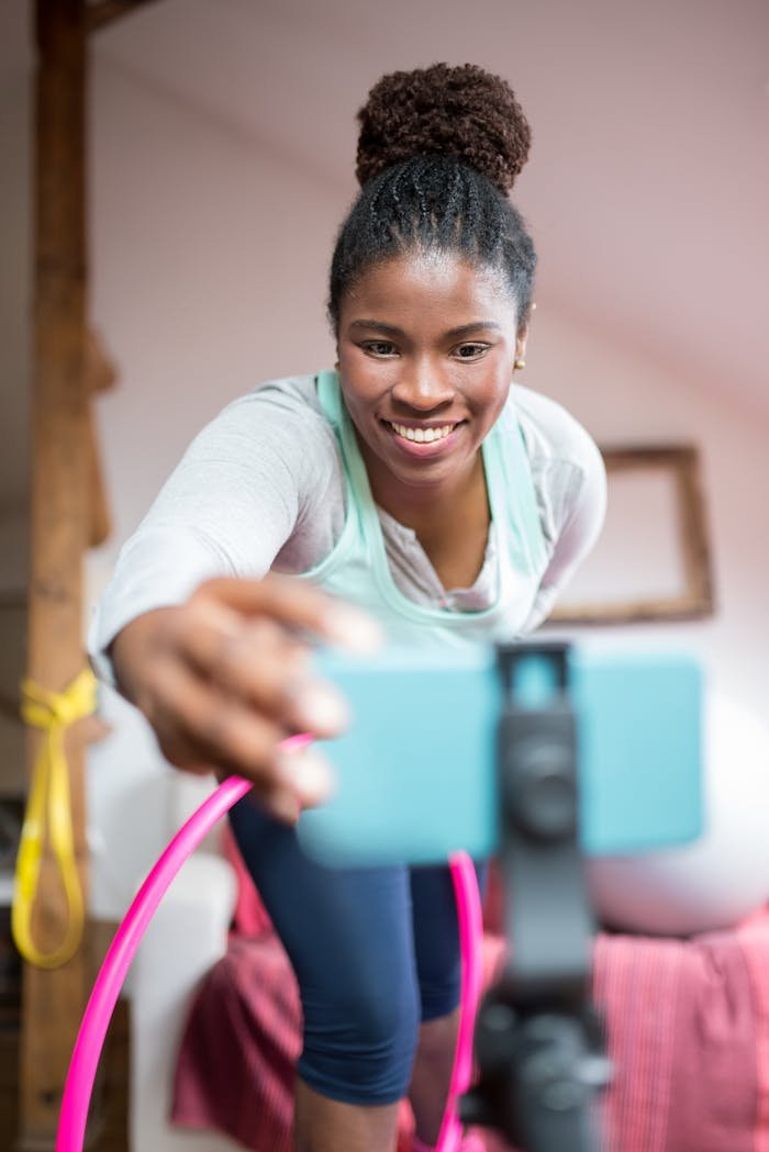 team-01 African American woman filming a fitness video with a smartphone indoors, smiling and engaged.